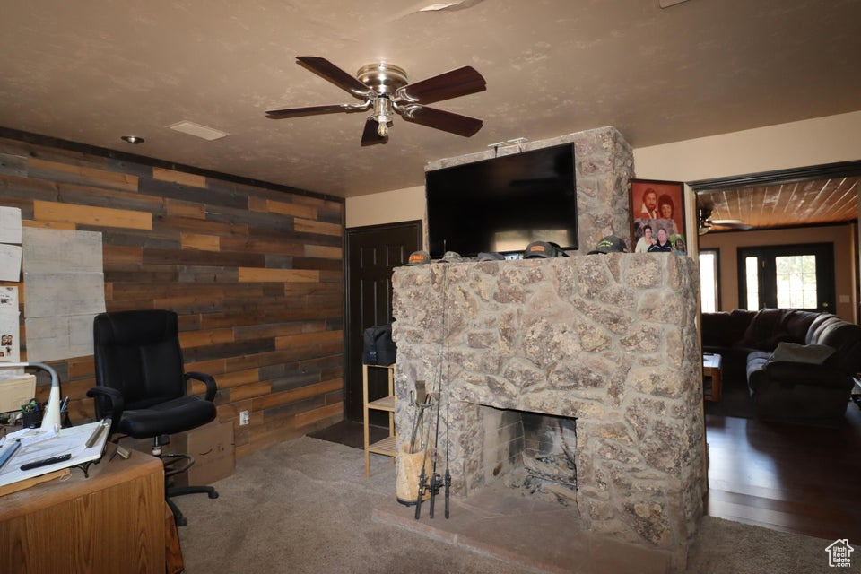 Carpeted living area with wooden walls, a ceiling fan, and a stone fireplace