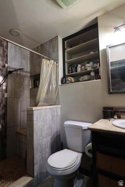 Full bath featuring a tile shower, tile walls, vanity, and toilet