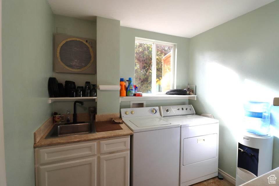 Clothes washing area with washing machine and clothes dryer, cabinet space, and a sink