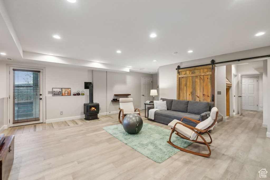 Living room with light wood-type flooring, a wood stove, a barn door, and baseboards