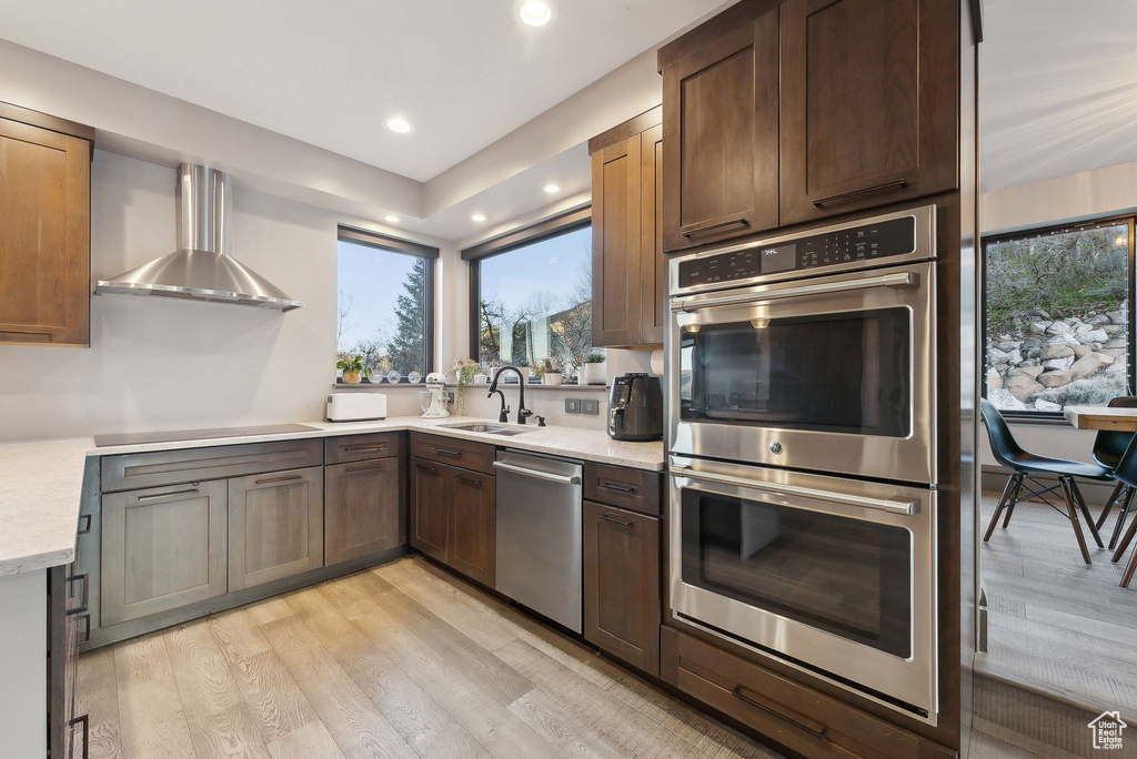 Kitchen featuring appliances with stainless steel finishes, recessed lighting, a sink, wall chimney exhaust hood, and light wood-type flooring