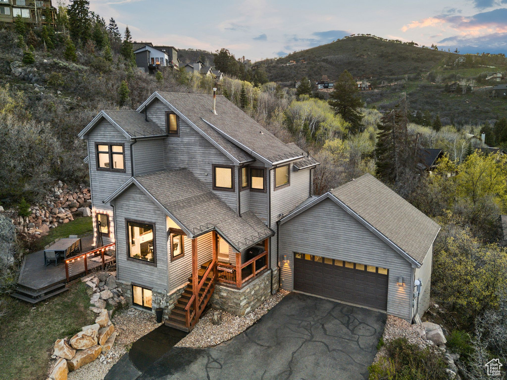 View of front of property with a deck with mountain view, a shingled roof, a garage, and aphalt driveway