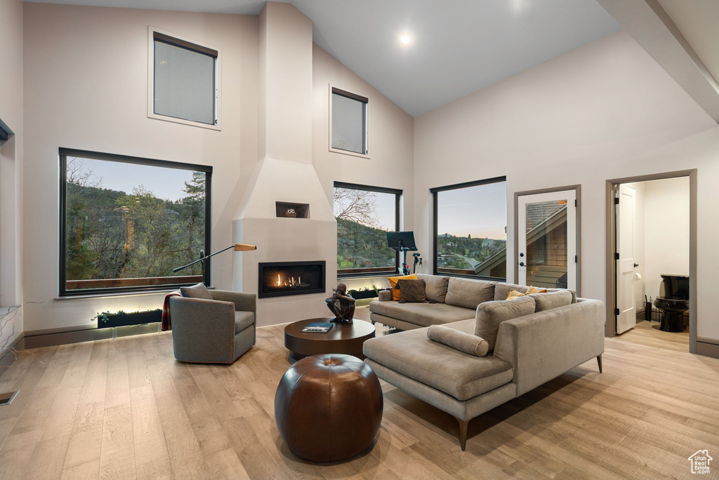 Living area with a large fireplace, visible vents, light wood-style flooring, and high vaulted ceiling