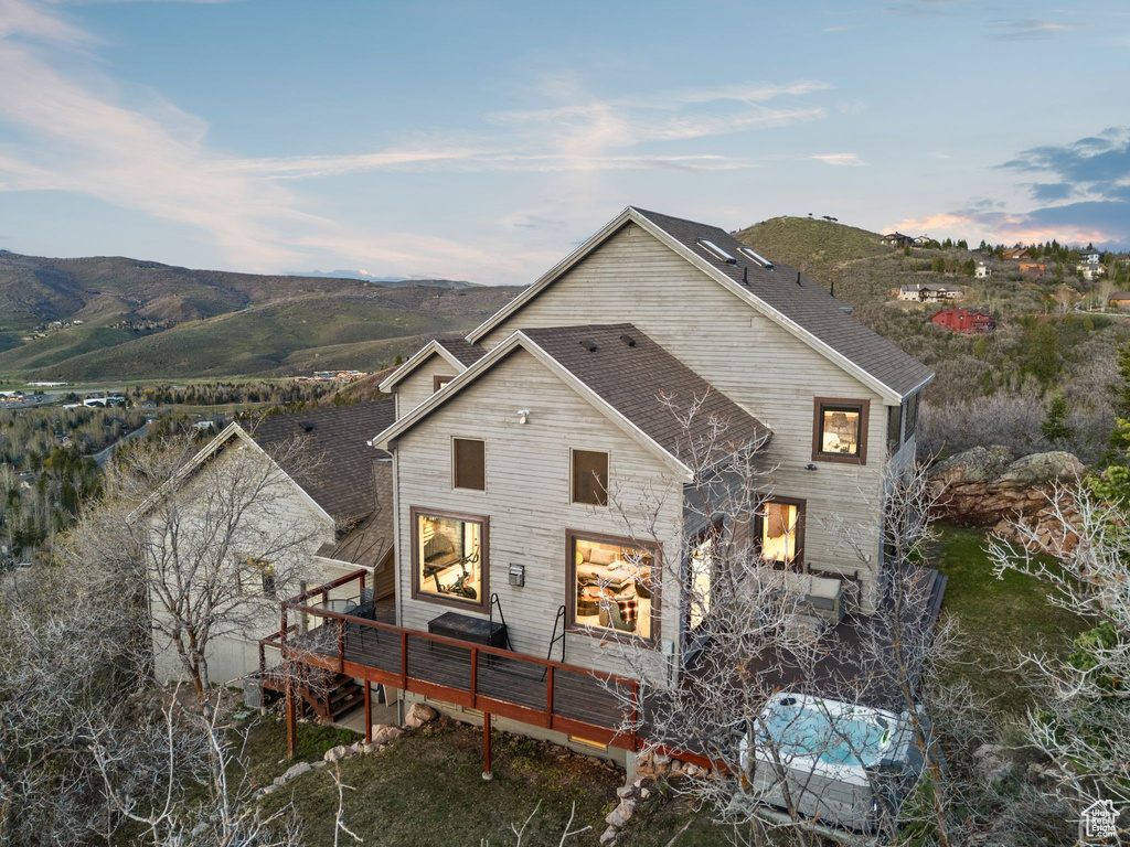 Back of property with a deck with mountain view and roof with shingles
