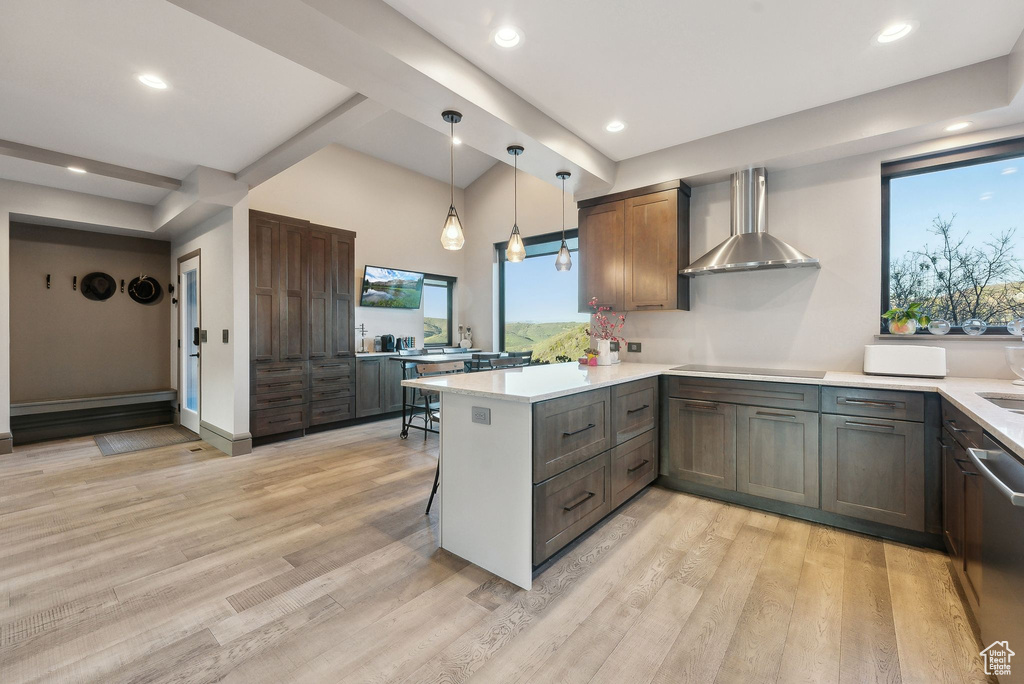 Kitchen featuring cooktop, a peninsula, wall chimney exhaust hood, light wood-style floors, and light countertops