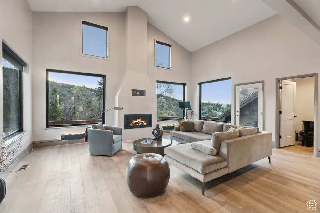 Living room with high vaulted ceiling, a fireplace, light wood-type flooring, visible vents, and recessed lighting