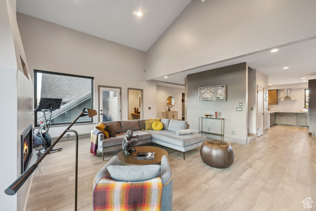 Living area with baseboards, light wood finished floors, recessed lighting, and high vaulted ceiling