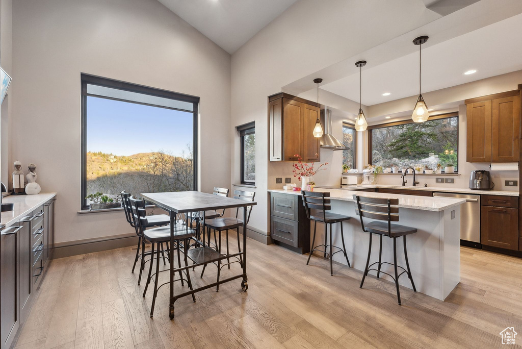 Kitchen featuring a breakfast bar area, a sink, stainless steel dishwasher, decorative light fixtures, and light wood-style floors