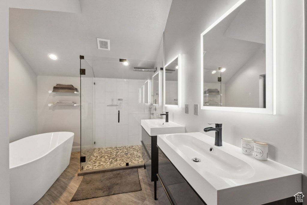 Full bathroom featuring wood finished floors, two vanities, a freestanding bath, visible vents, and a shower stall