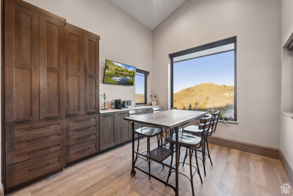 Dining room with high vaulted ceiling, baseboards, and light wood-type flooring