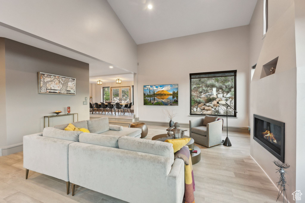 Living room with light wood-type flooring, baseboards, a glass covered fireplace, and high vaulted ceiling