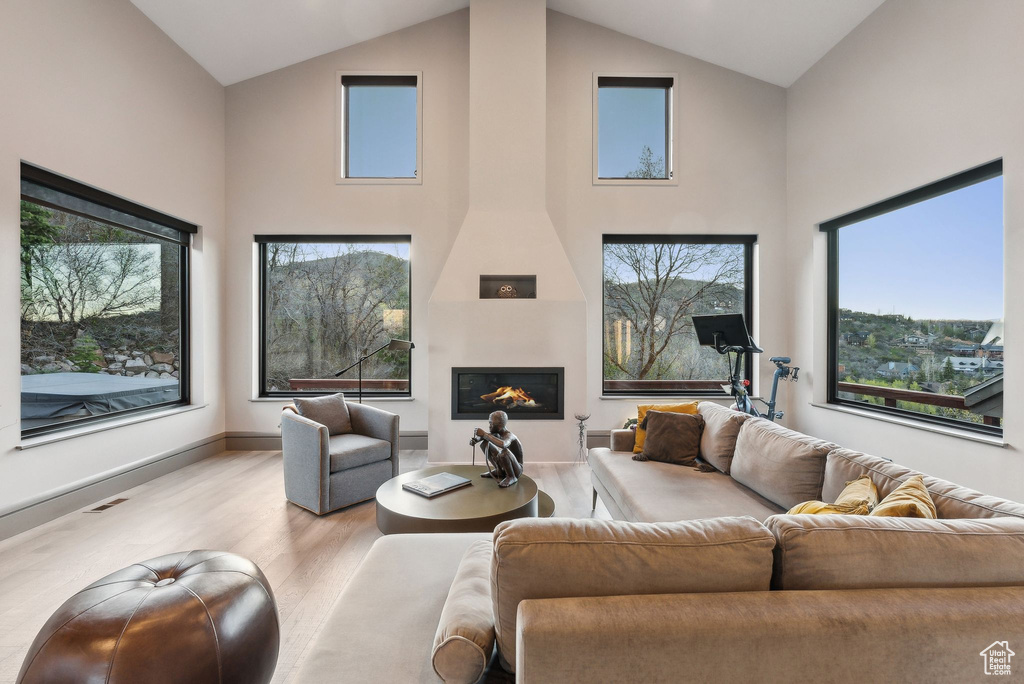 Living area with a large fireplace, wood finished floors, a healthy amount of sunlight, and high vaulted ceiling