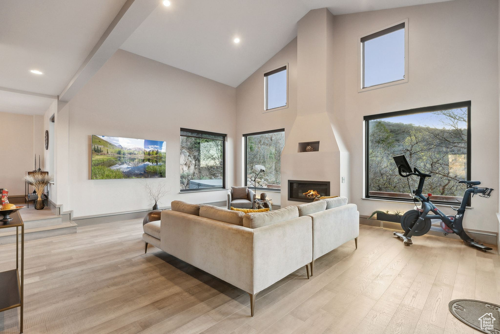 Living room with a fireplace, high vaulted ceiling, plenty of natural light, and light wood-style floors