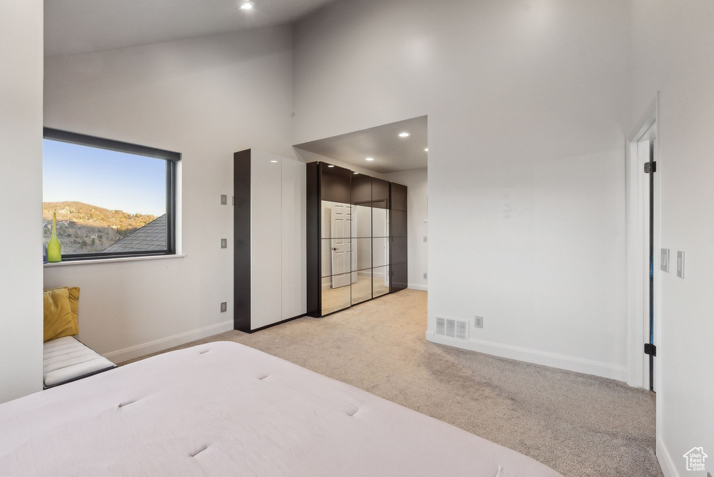 Bedroom featuring light colored carpet, a towering ceiling, visible vents, recessed lighting, and baseboards