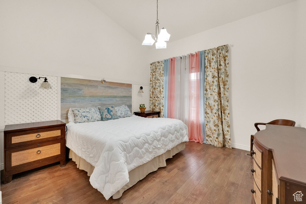 Bedroom featuring baseboards, a notable chandelier, wood finished floors, and high vaulted ceiling