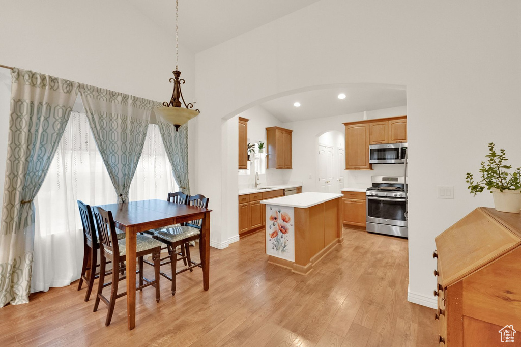 Kitchen with appliances with stainless steel finishes, light countertops, arched walkways, light wood-style flooring, and a center island