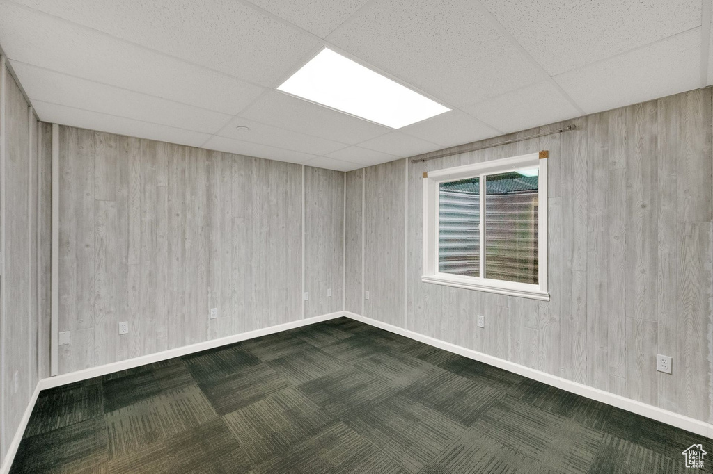 Unfurnished room featuring baseboards, a drop ceiling, and wooden walls