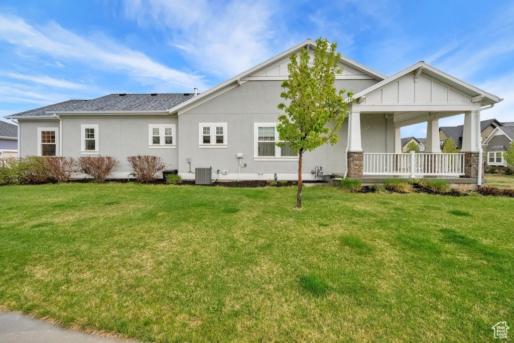 Rear view of house featuring a porch, central AC unit, a lawn, and stucco siding