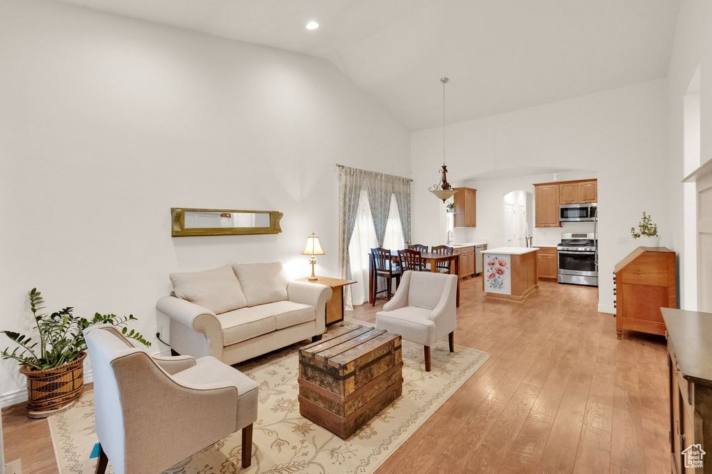 Living room featuring arched walkways, high vaulted ceiling, recessed lighting, and light wood finished floors