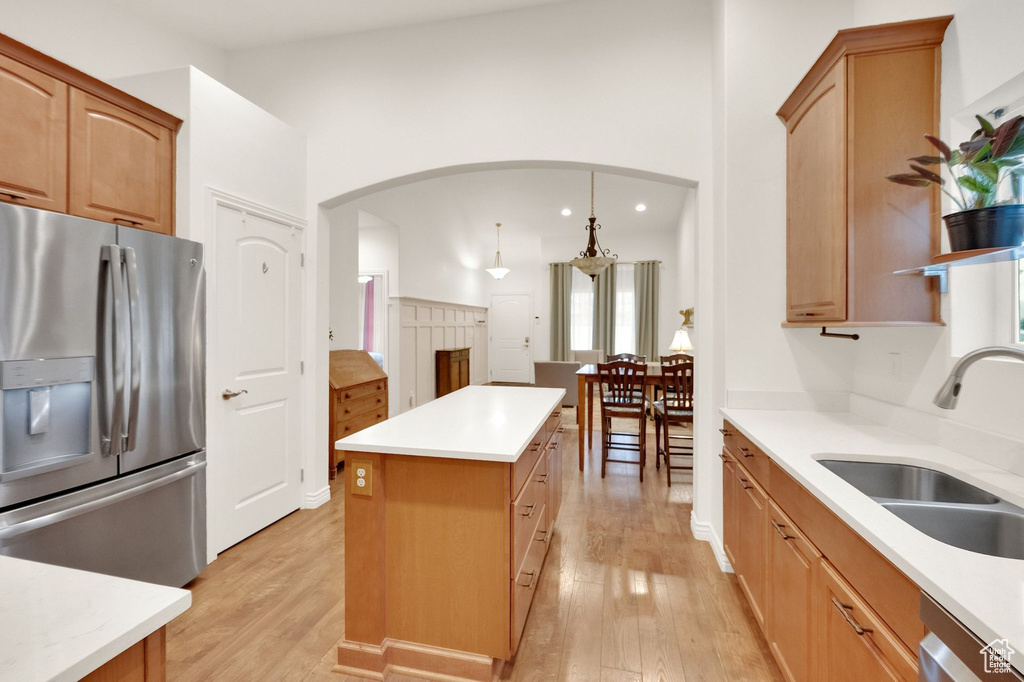 Kitchen with appliances with stainless steel finishes, arched walkways, a center island, a sink, and light wood-style floors