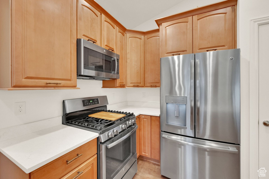 Kitchen with light countertops, light brown cabinets, stainless steel appliances, and lofted ceiling