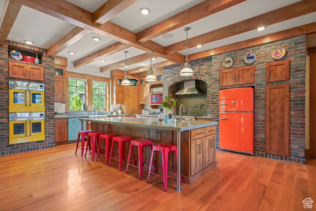 Kitchen featuring light wood finished floors, dishwashing machine, refrigerator, white microwave, and wall chimney range hood