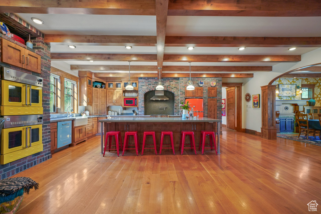 Kitchen featuring a kitchen bar, pendant lighting, double oven, beamed ceiling, and light wood-style floors