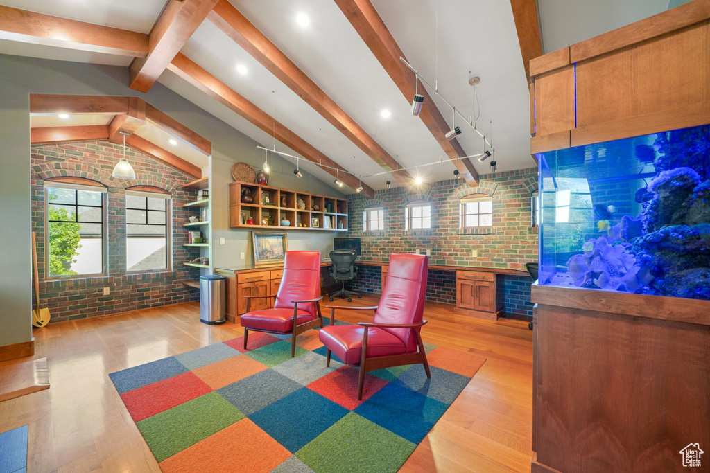 Interior space with a wood stove, brick wall, light wood-type flooring, and vaulted ceiling with beams