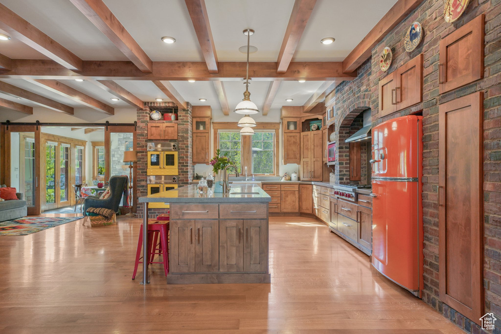Kitchen with freestanding refrigerator, light wood finished floors, open floor plan, a sink, and beam ceiling