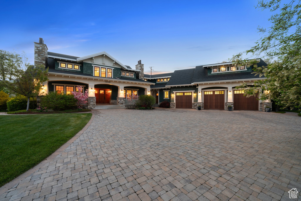 View of front of home with a chimney, stone siding, a yard, and decorative driveway