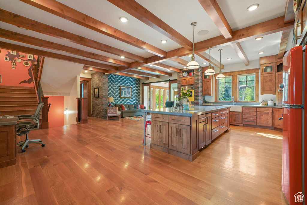 Kitchen featuring a breakfast bar, stainless steel counters, brown cabinetry, open floor plan, and light wood-type flooring