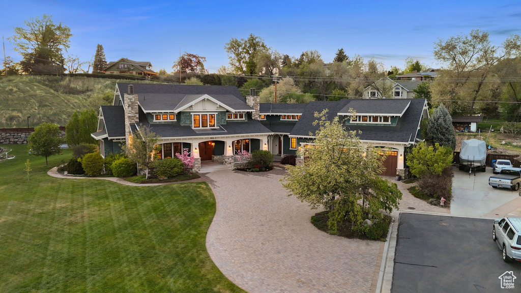 Shingle-style home with a chimney, decorative driveway, a shingled roof, a porch, and a front lawn