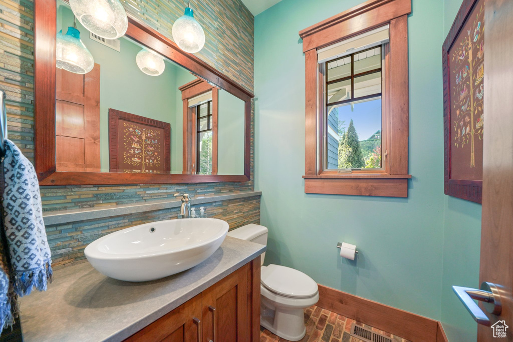 Half bathroom featuring toilet, brick floor, visible vents, decorative backsplash, and baseboards