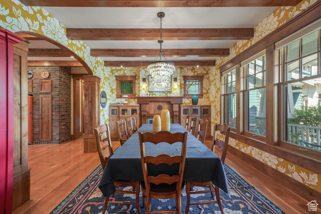 Dining space featuring arched walkways, light wood-style flooring, beamed ceiling, and a chandelier
