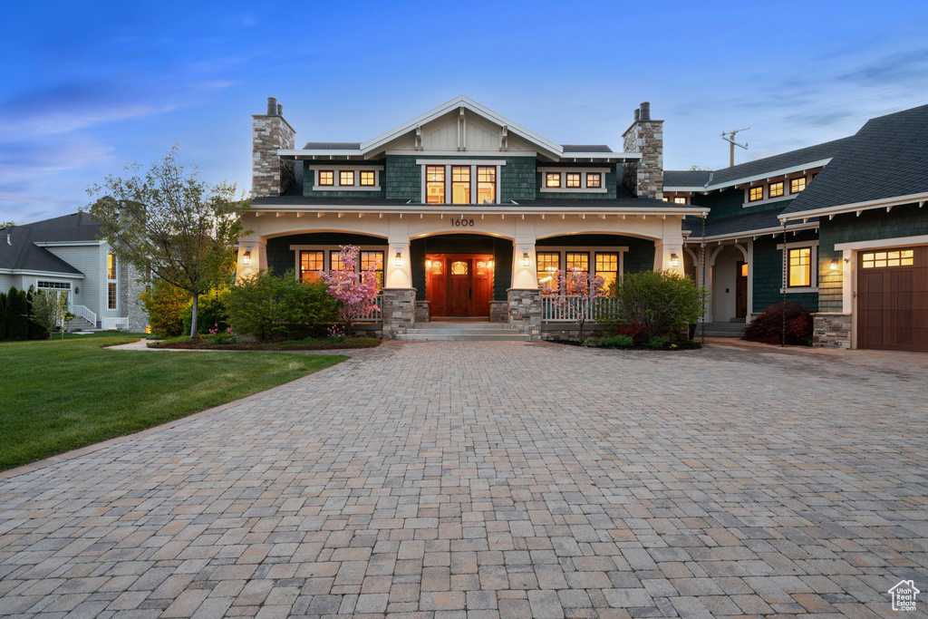 View of front of home featuring stone siding, decorative driveway, a chimney, and a porch