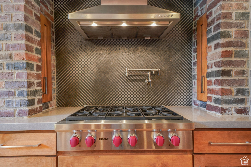 Kitchen with stainless steel gas cooktop, wall chimney range hood, light countertops, and decorative backsplash