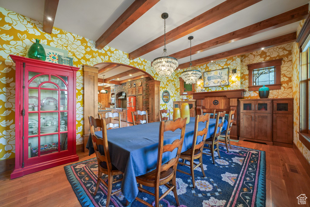 Dining space featuring a notable chandelier, wallpapered walls, wood finished floors, arched walkways, and beam ceiling