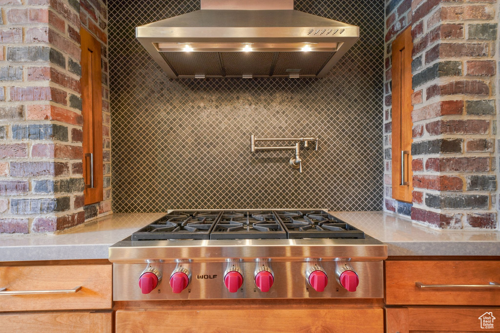 Kitchen with light countertops, stainless steel gas stovetop, decorative backsplash, and wall chimney exhaust hood