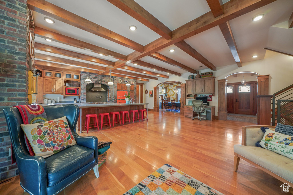 Living area featuring arched walkways, decorative columns, beamed ceiling, light wood-style flooring, and recessed lighting