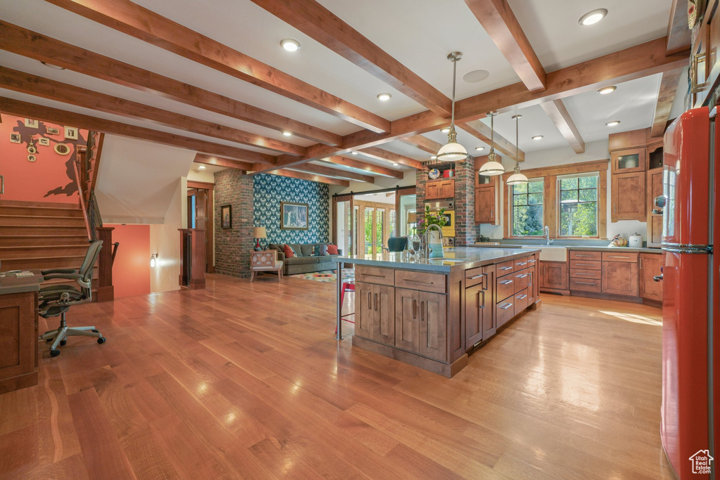 Kitchen featuring open floor plan, brown cabinetry, a kitchen breakfast bar, light wood finished floors, and beamed ceiling