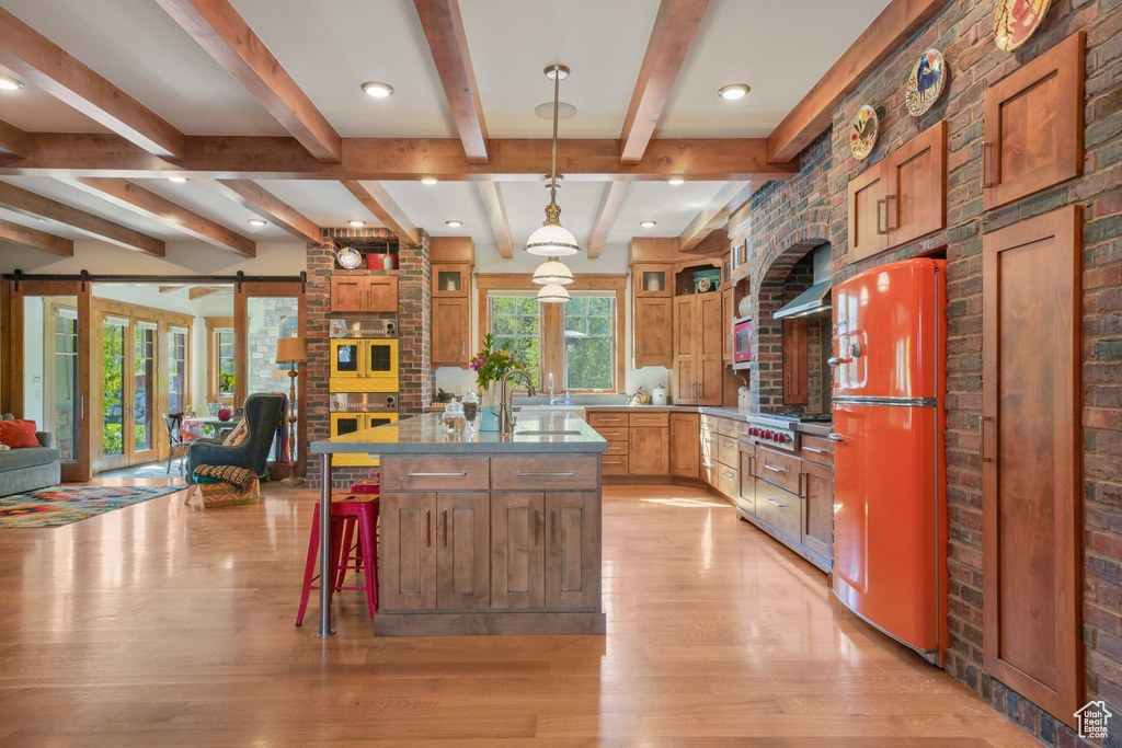 Kitchen with fridge, a barn door, an island with sink, light wood finished floors, and open floor plan