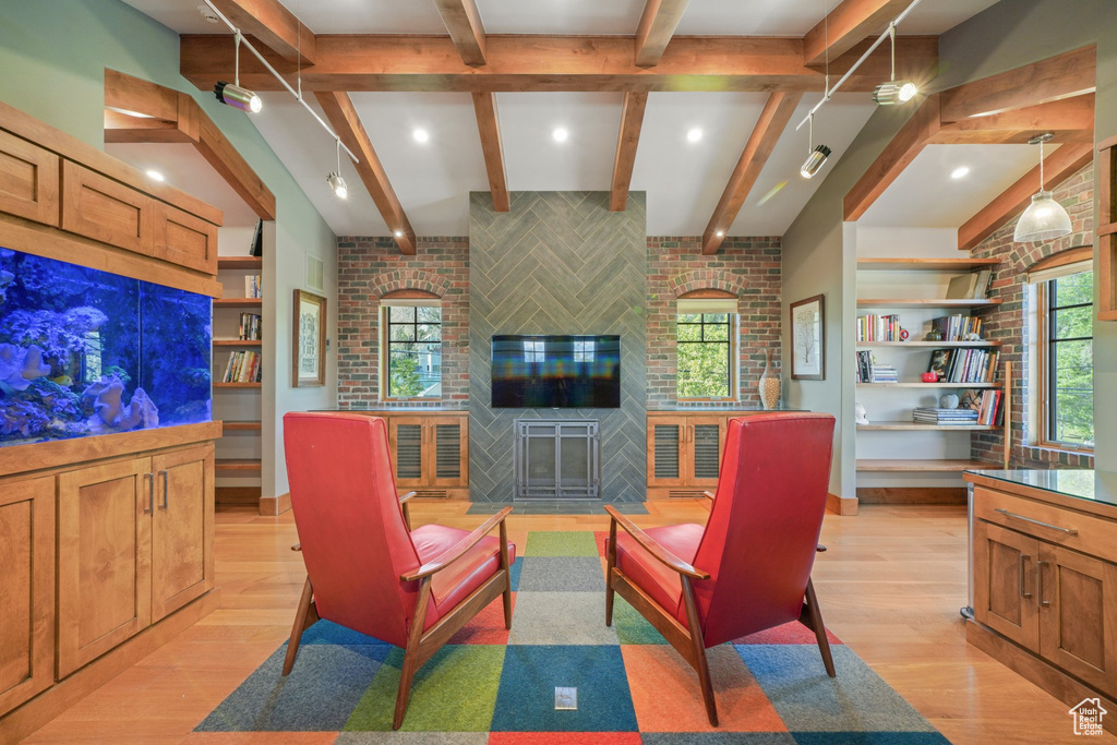 Living area featuring brick wall, healthy amount of natural light, light wood-style flooring, and beamed ceiling