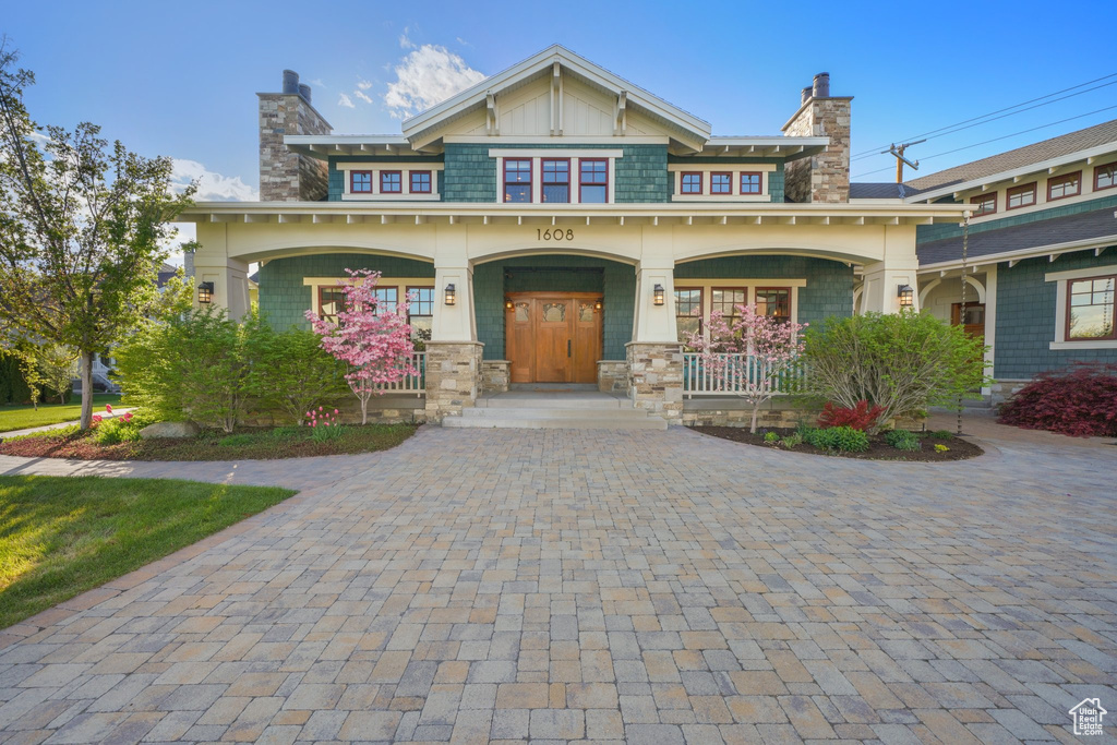 Craftsman house with covered porch, decorative driveway, and a chimney