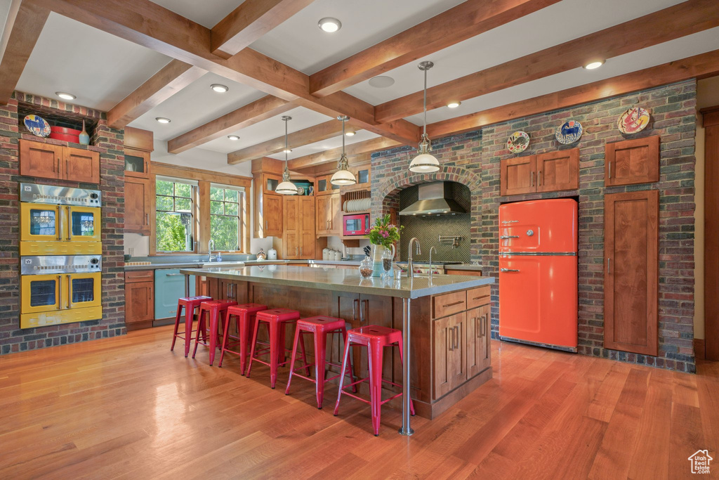 Kitchen with refrigerator, light wood finished floors, wall chimney range hood, dishwashing machine, and double oven