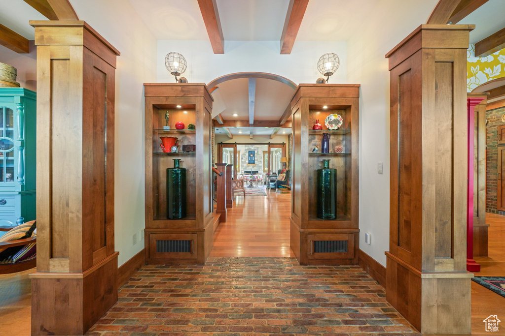 Hallway with brick floor, ornate columns, beamed ceiling, and arched walkways