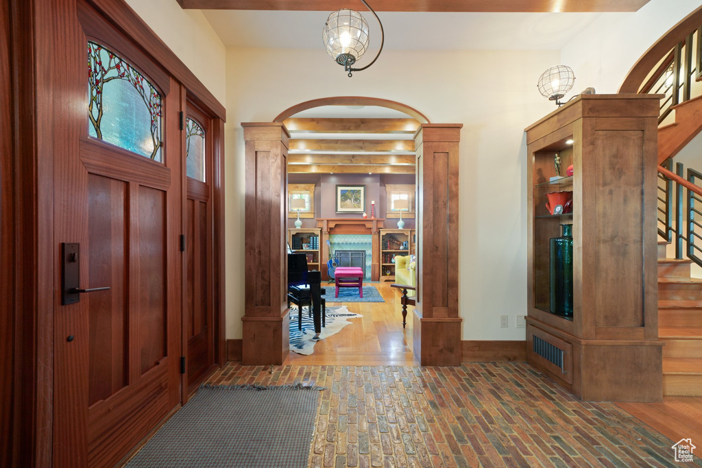 Foyer featuring brick floor, arched walkways, stairway, a fireplace, and ornate columns