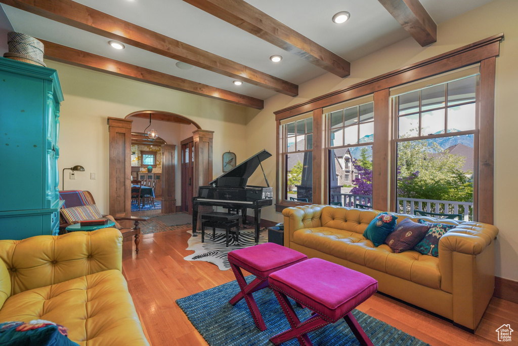 Living area with arched walkways, decorative columns, wood finished floors, beamed ceiling, and recessed lighting