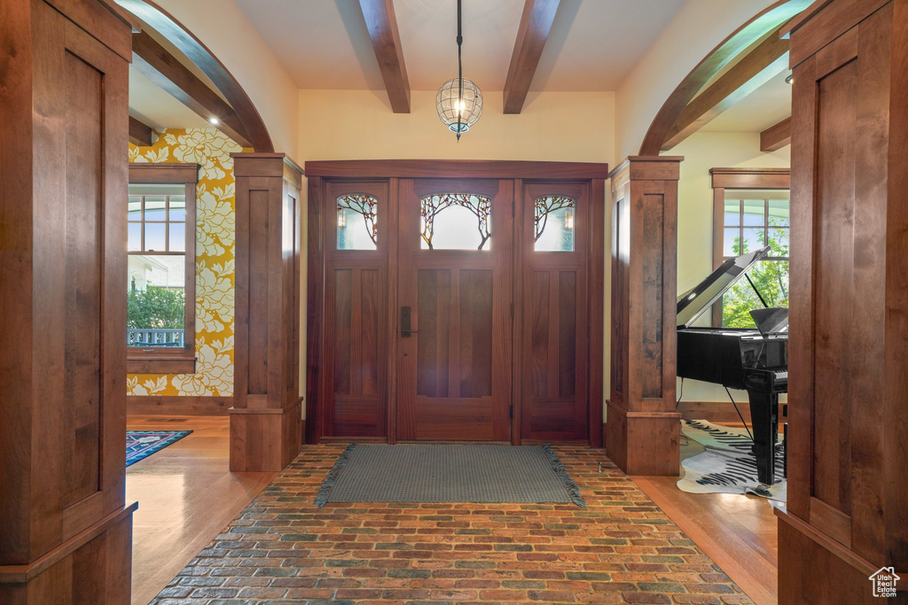 Entrance foyer featuring beam ceiling, brick floor, and decorative columns