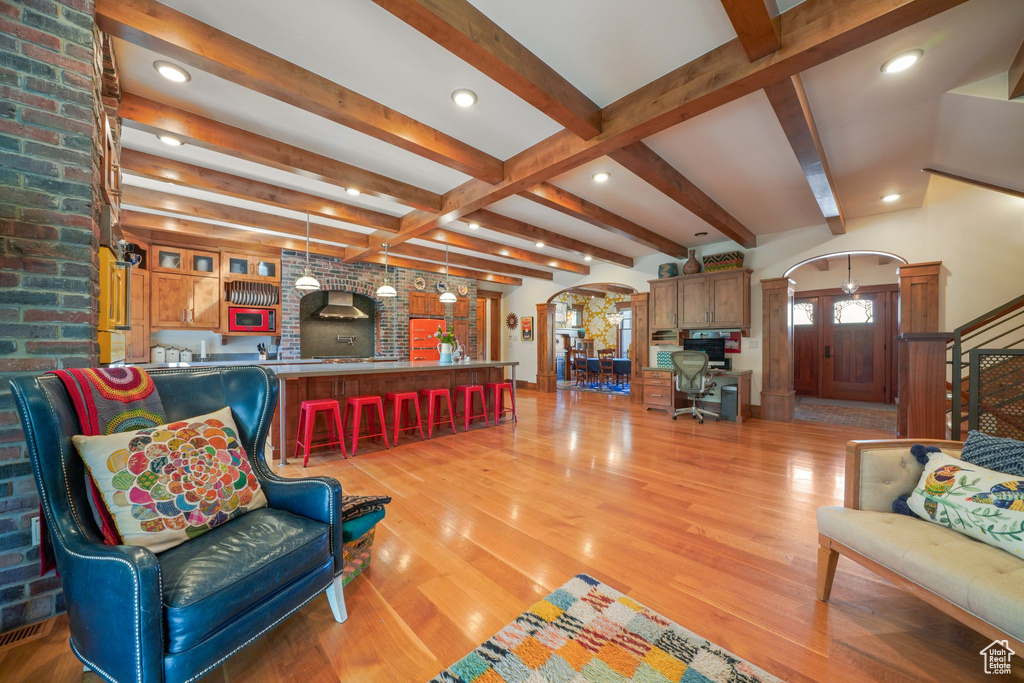 Living area featuring beam ceiling, light wood-type flooring, ornate columns, recessed lighting, and arched walkways