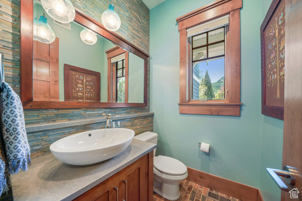 Half bathroom featuring baseboards, toilet, brick flooring, tasteful backsplash, and vanity